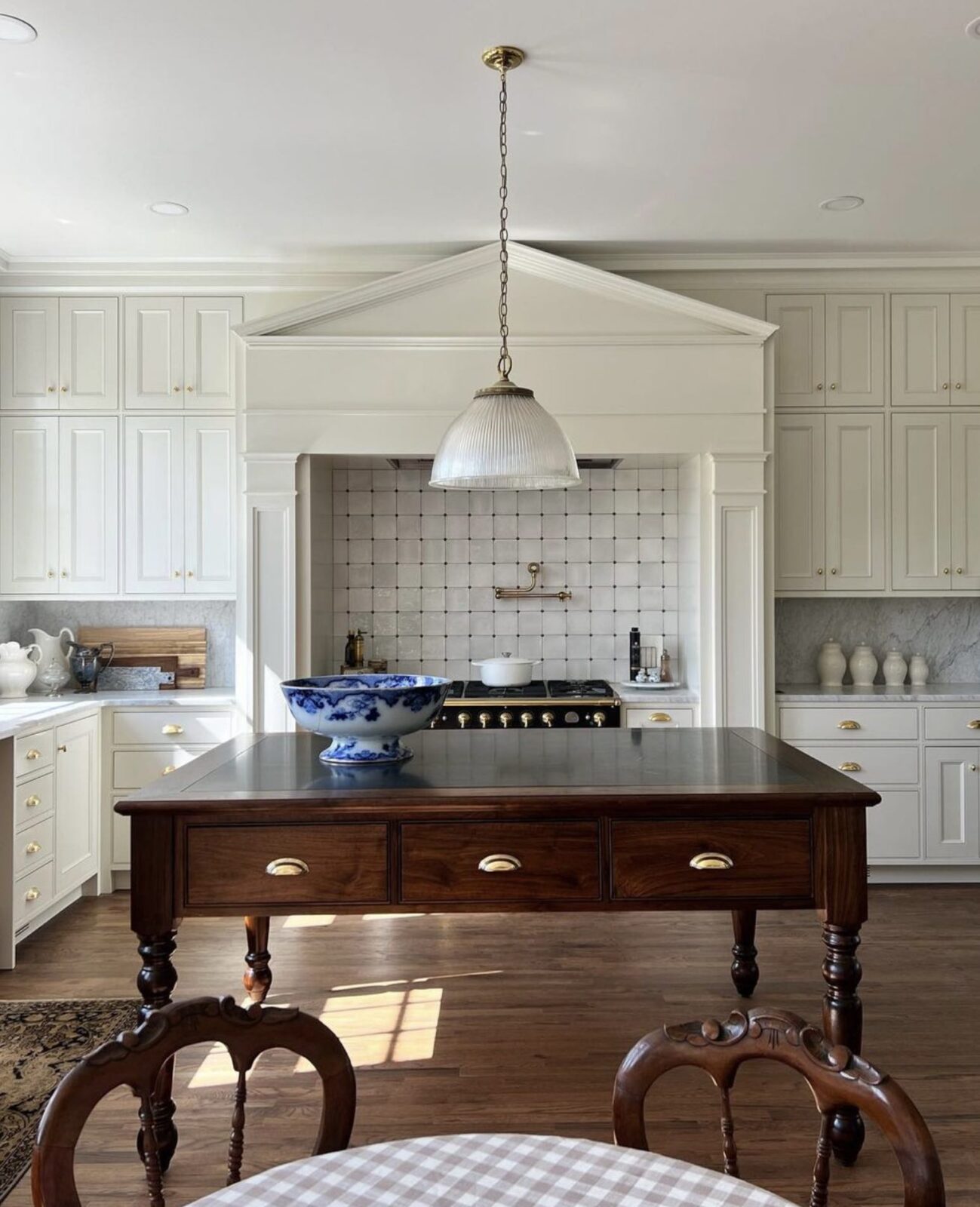White kitchen with marble countertops, wood floors, and an antique wood island