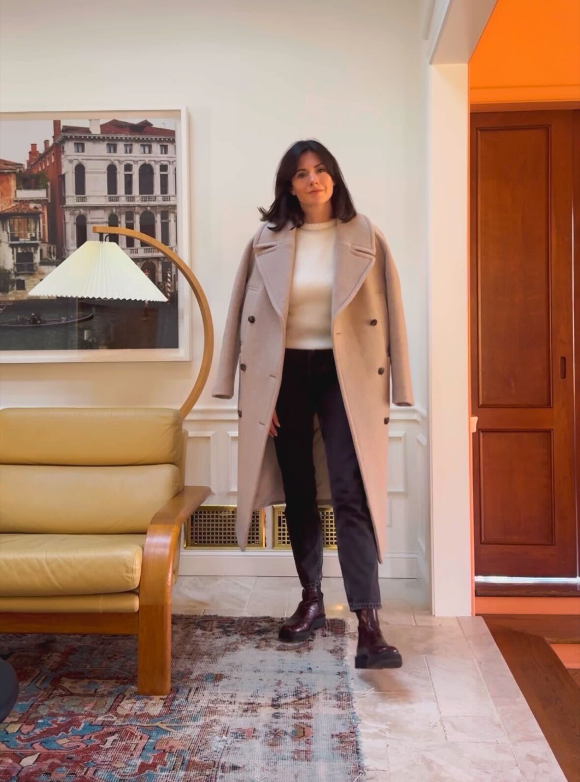 Woman wearing a white sweater, long Sézane wool coat, black jeans, and Chelsea boots