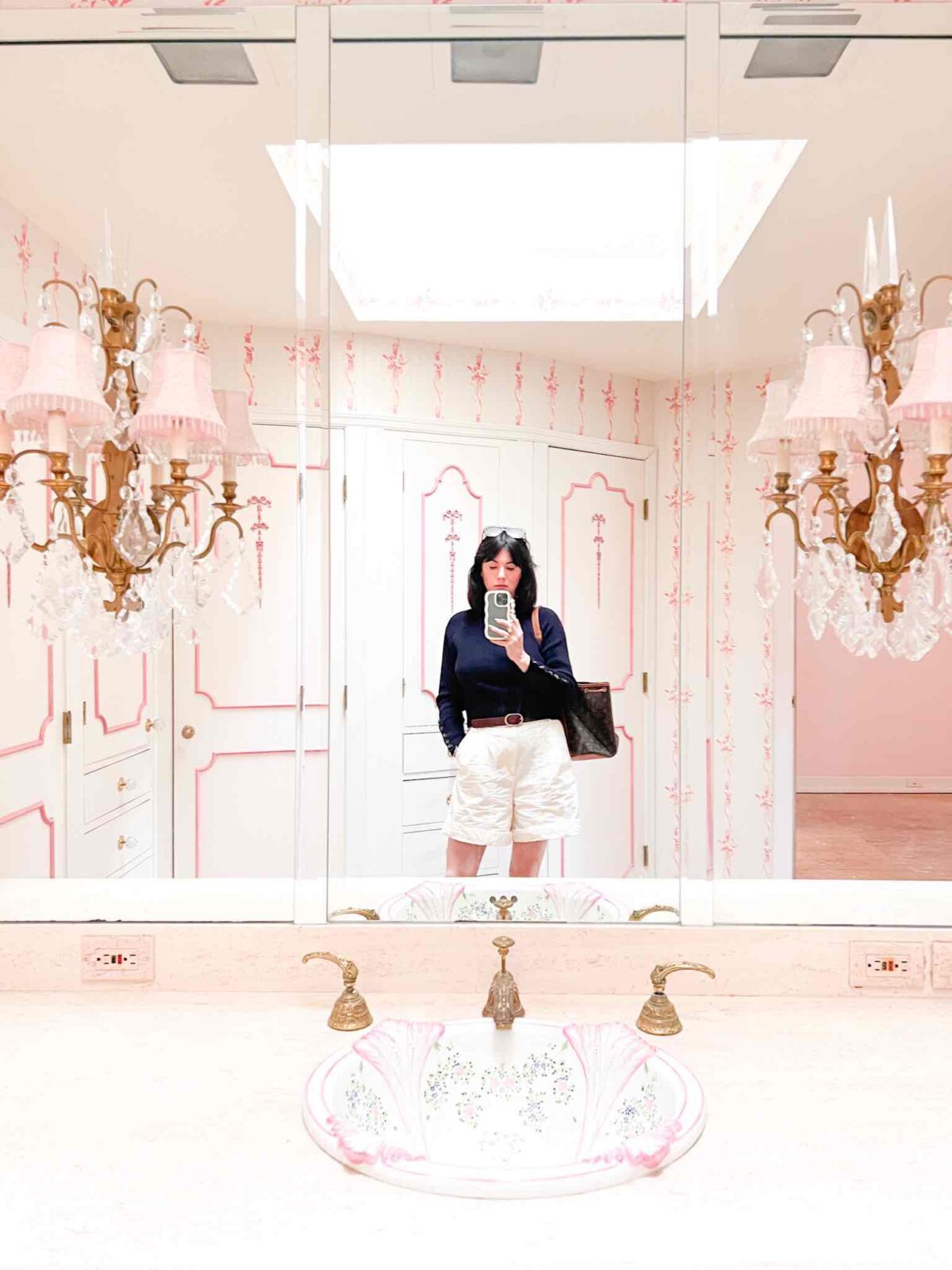 Bathroom with pink design details on the wallpaper and woodwork, ornate gold sconces, and a skylight