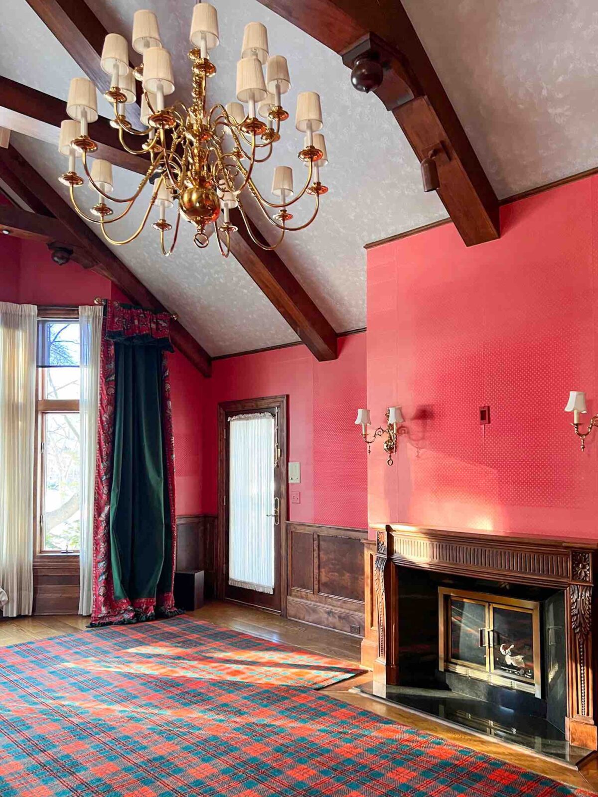 Room with high beamed ceilings, a large chandelier, red wallpaper, and a red and green rug