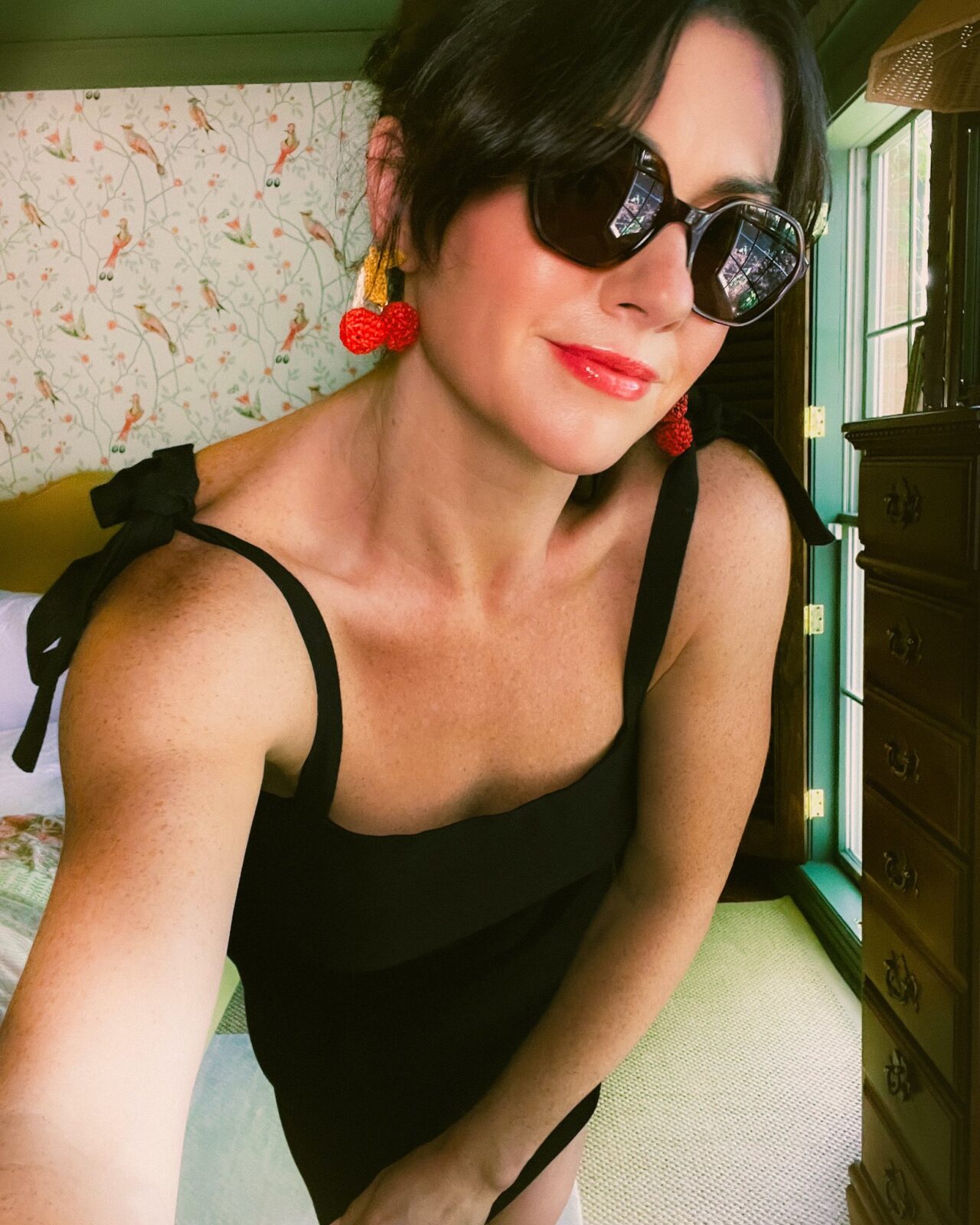 Woman wearing the perfect little black dress from Sézane, cherry-shaped earrings, and black sunglasses