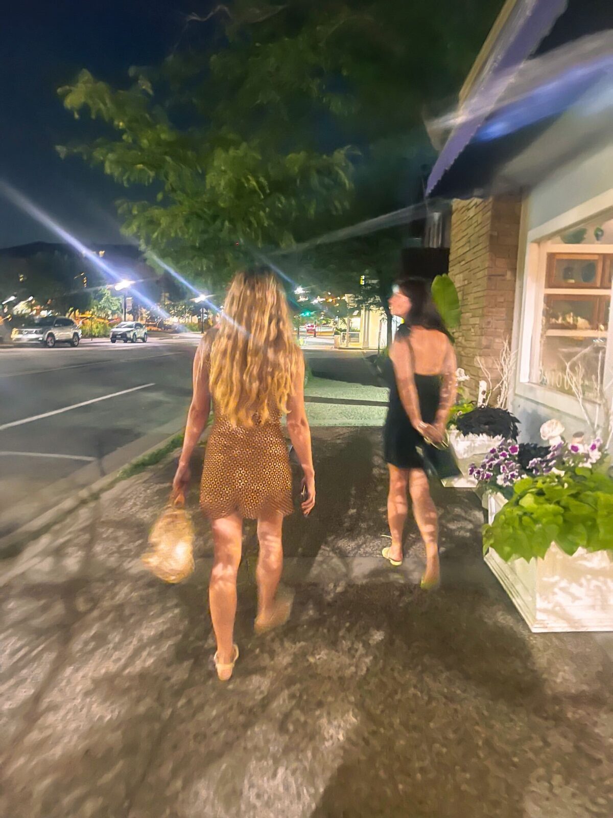 Two women wearing dresses shown walking down a city sidewalk at night