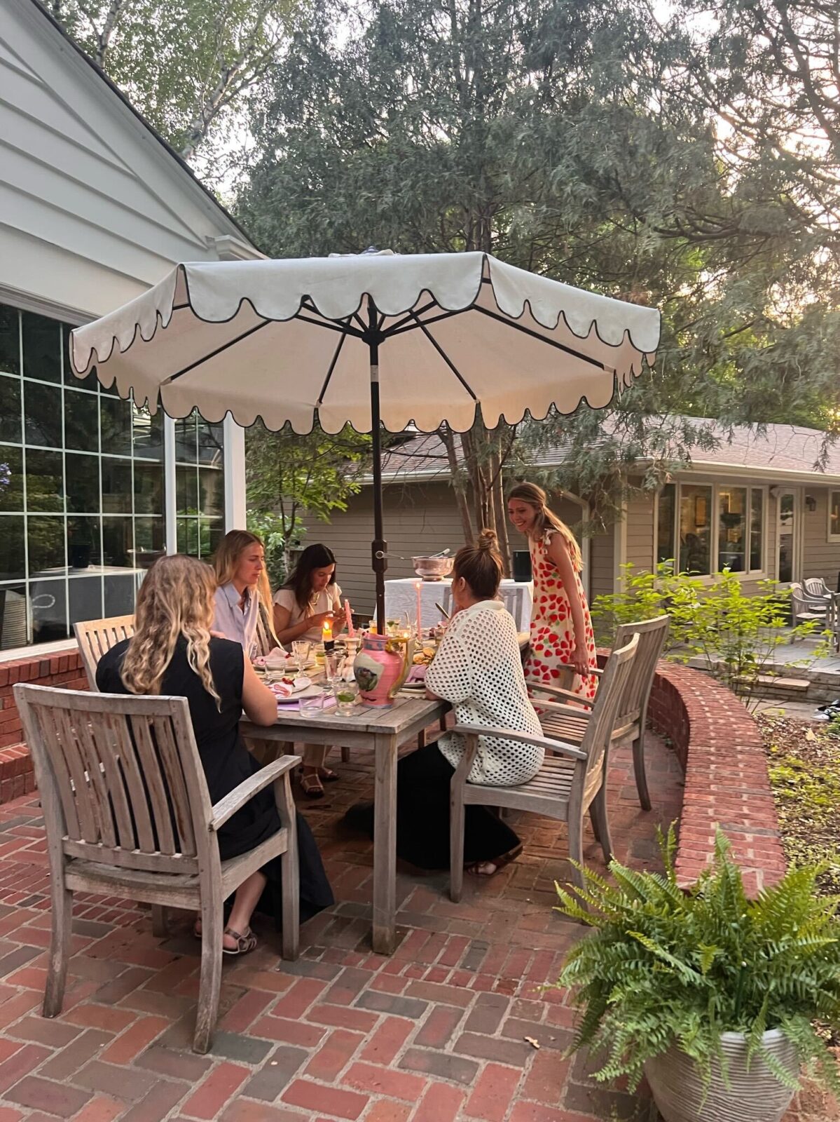 Friends are seated at an outdoor dining table for dinner on a summer evening