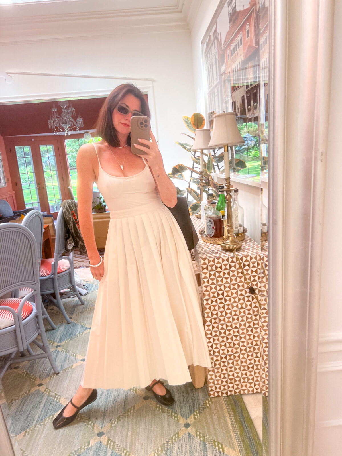 A woman standing in her dining room wearing a white Target dress, black J. Crew flats, and sunglasses