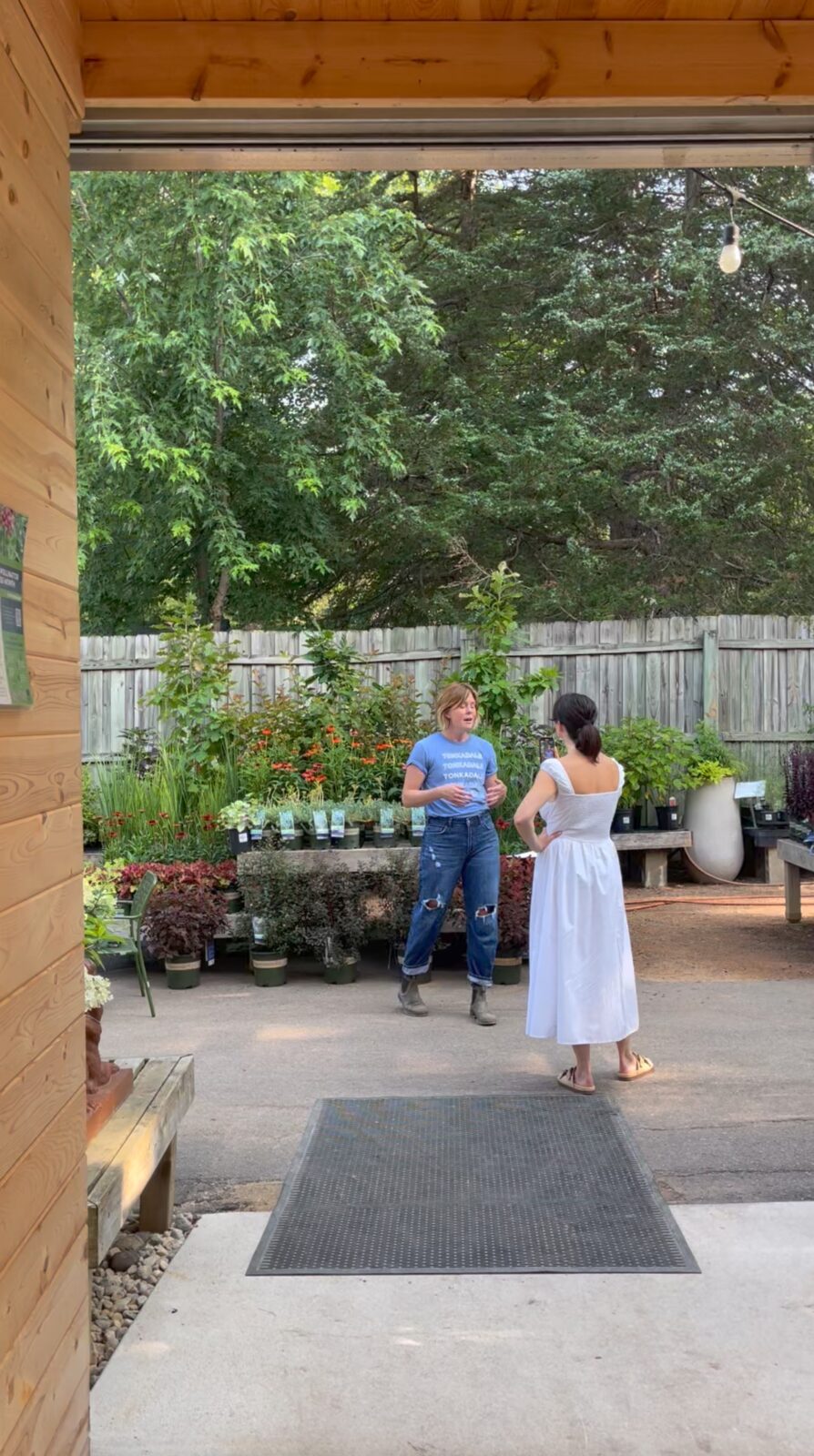 Two women walking through a gardening and landscaping nursery looking at plants