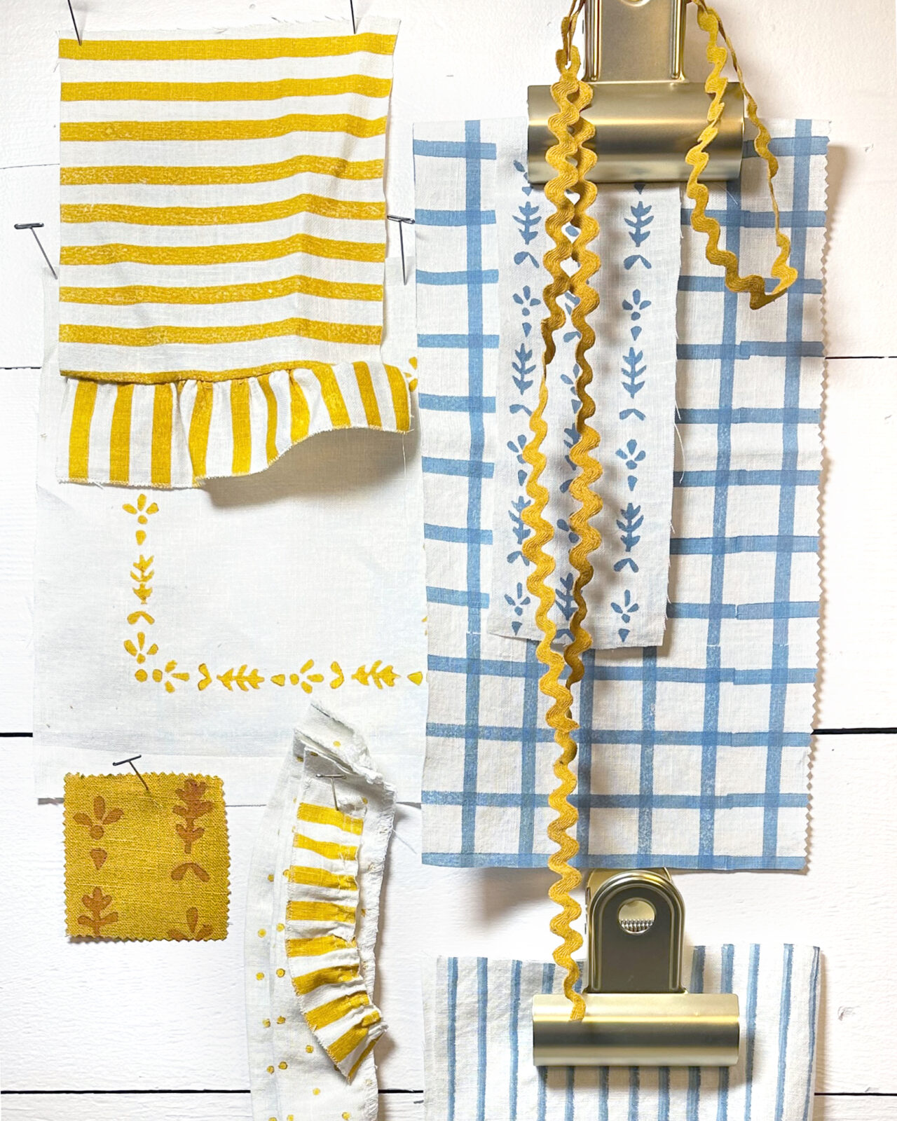 A variety of fabric samples in blue, yellow, and white colors are pinned up on a wall.