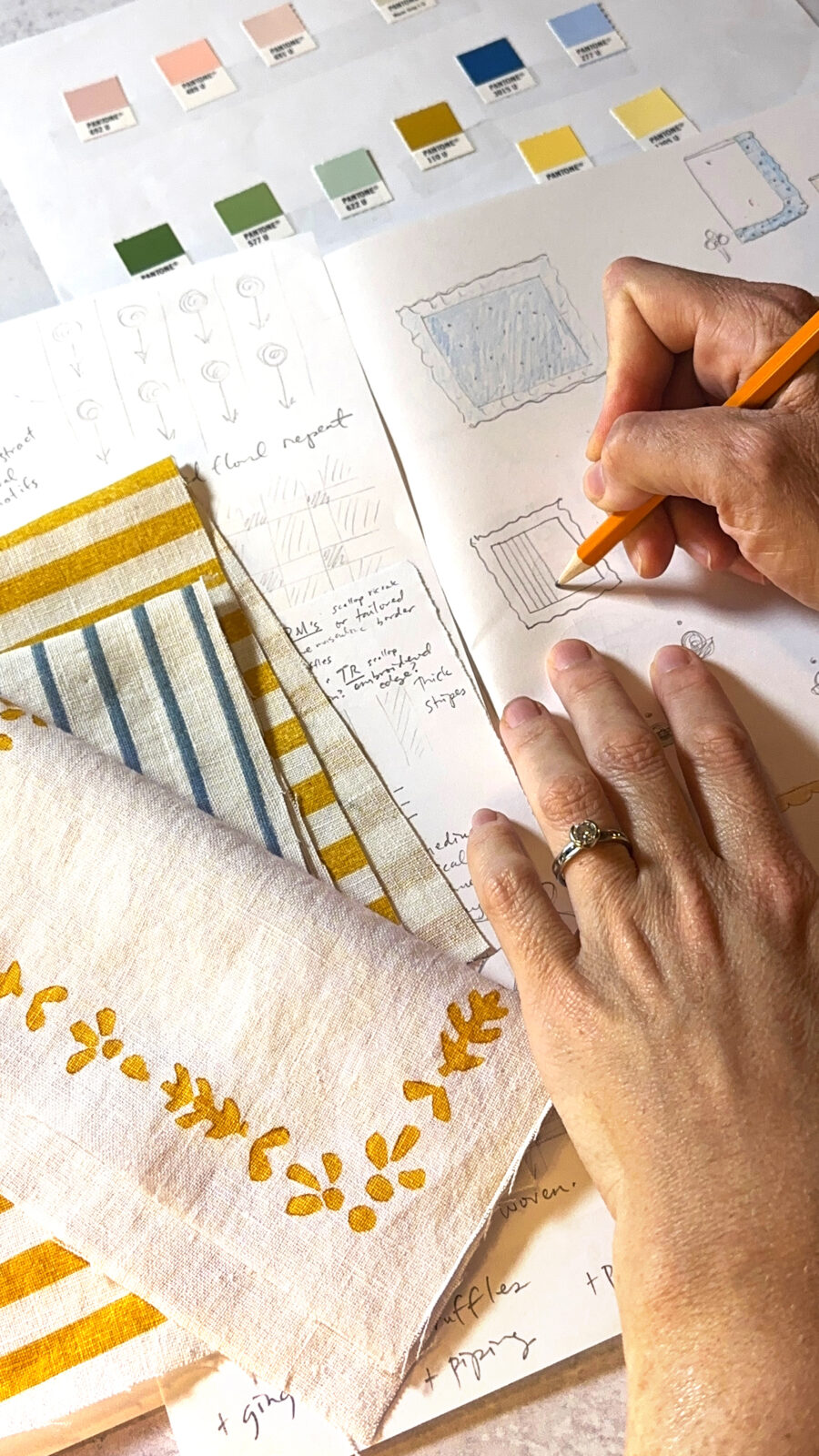 Hands are shown drawing designs for tabletop linens on paper. Color swatches and fabric samples are also in the frame.