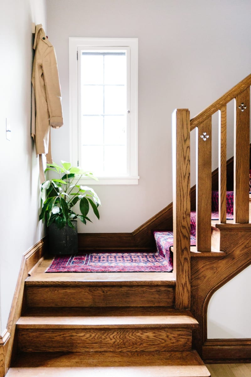 Wood staircase covered with a vintage stair runner, with a plant on the landing.